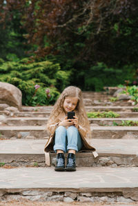 Caucasian girl of seven years old sits on stone steps in a park and communicates online with friends