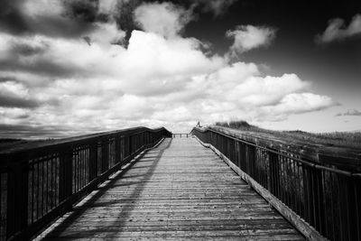 Footbridge against cloudy sky during sunny day