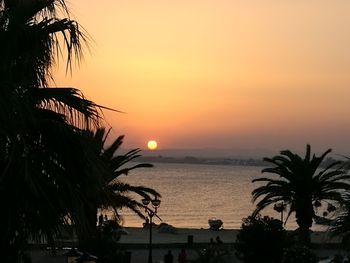 Silhouette palm trees by sea against romantic sky at sunset