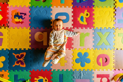 Directly above portrait of cute baby girl lying on colorful alphabets