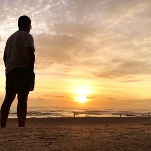 Rear view of silhouette mature man standing at beach against sky during sunset