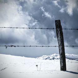 Fence on snow covered field against sky