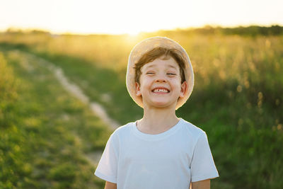 Portrait of a smiling little boy in a white t-shirt and hat playing outdoors on the field at sunset