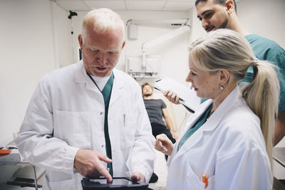 Doctors discussing over digital tablet while patient lying on bed at hospital