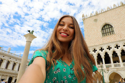 Portrait of smiling young woman against building