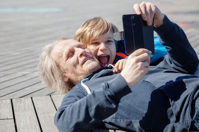 Grandfather and grandson taking selfie while lying down outdoors