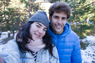 Portrait of young couple wearing warm clothing standing in forest during winter
