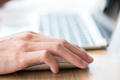 Cropped hand of man using laptop at table