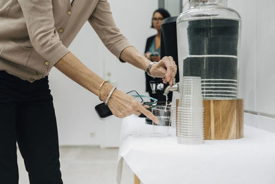 Midsection of mature entrepreneur filling water in glass