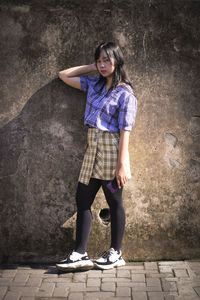 Full length portrait of a woman standing against wall