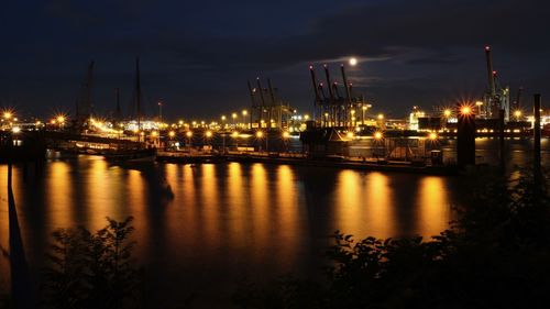 Illuminated factory by river against sky at night