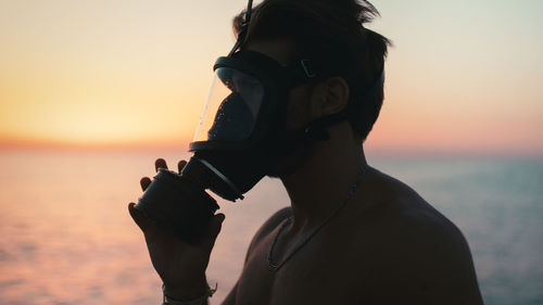 Silhouette of a boy putting on his gas mask at dawn in the ocean
