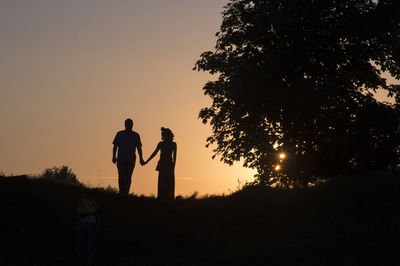 Silhouette couple holding hands while standing on field against sky during sunset