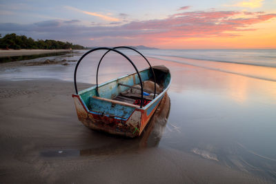 Boat moored on beach against sky during sunset