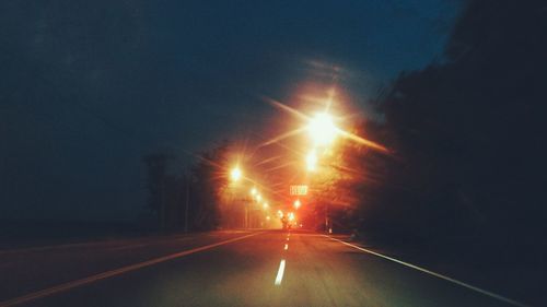 Illuminated road against sky at night