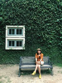 Woman sitting on bench against plants