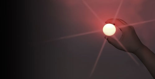 Close-up of hand holding illuminated lighting equipment against sky