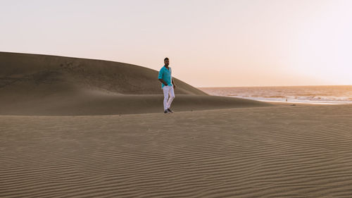 Rear view of woman walking at beach against clear sky