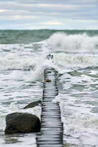 Scenic view of blue sea with bubbling and foaming waves. vintage long wooden breakwaters in sea