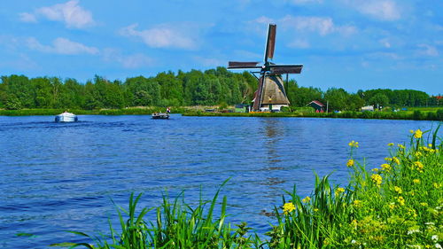 Traditional windmill by lake against sky