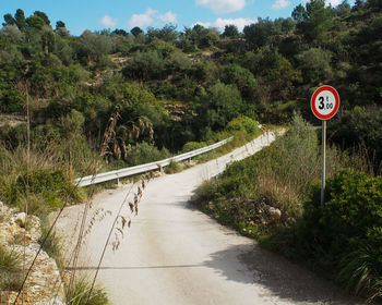 Road sign by trees against sky