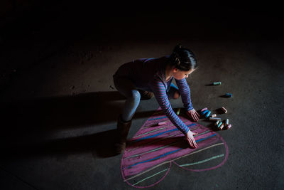 High angle view of girl making heart shape with chalk on floor