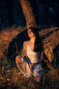 Portrait of young woman sitting on tree trunk in forest