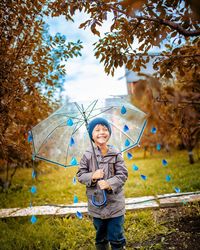 Portrait of smiling woman standing by tree on field