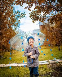 Smiling boy standing with umbrella by tree