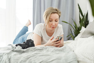 Young woman using mobile phone while sitting on bed