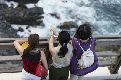 Rear view of female friends standing on footbridge over sea