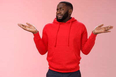 Young man with arms raised standing against red background