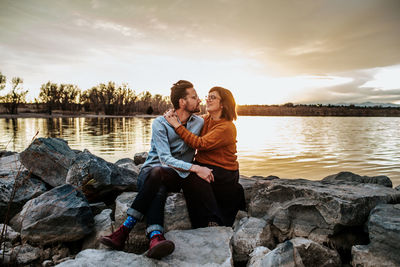 Husband and wife sitting on rocks near a lake on a autumn evening