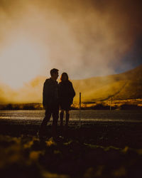 Silhouette couple standing on field against sky during sunset