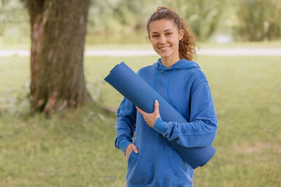 A european woman in a blue hoodie with a blue yoga mat chooses a place to do sports and meditation