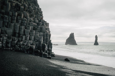 Rock formation at beach against cloudy sky