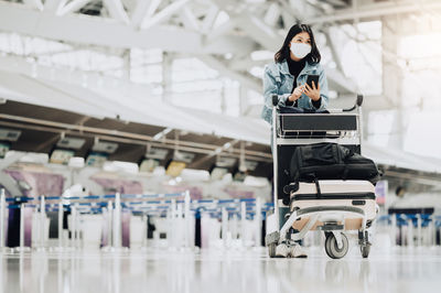 Woman with suitcase in trolley using phone while standing at airport