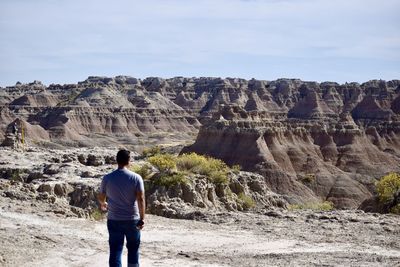 Rear view of man standing on rock against sky