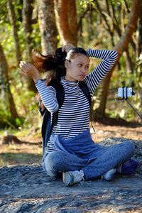 Young woman tying hair while sitting on rock in forest