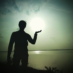 Silhouette man standing at beach against sky during sunset