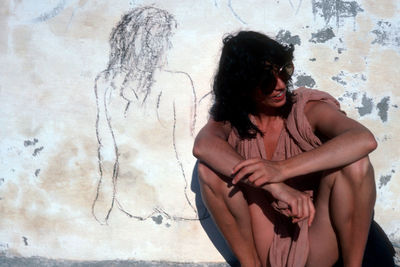 Young woman sitting against wall