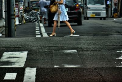 Low section of woman walking on road in city