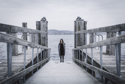 Rear view of man standing on railing by sea against sky