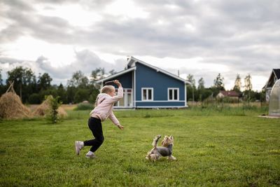 Full length of girl with dog playing on grass against sky