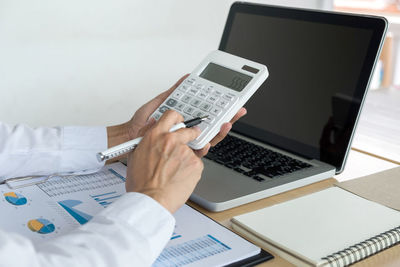 Cropped hands of businessman calculating at desk in office