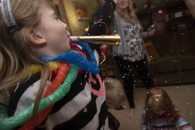 Girl blowing party horn blower during celebration in living room at home