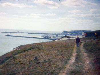 Rear view of man walking on beach against sky