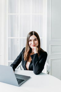 Portrait of young woman using phone while sitting on table