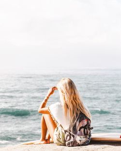 Young woman sitting on beach against sky