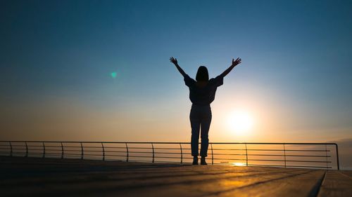 Silhouette woman standing on pier against clear sky during sunset